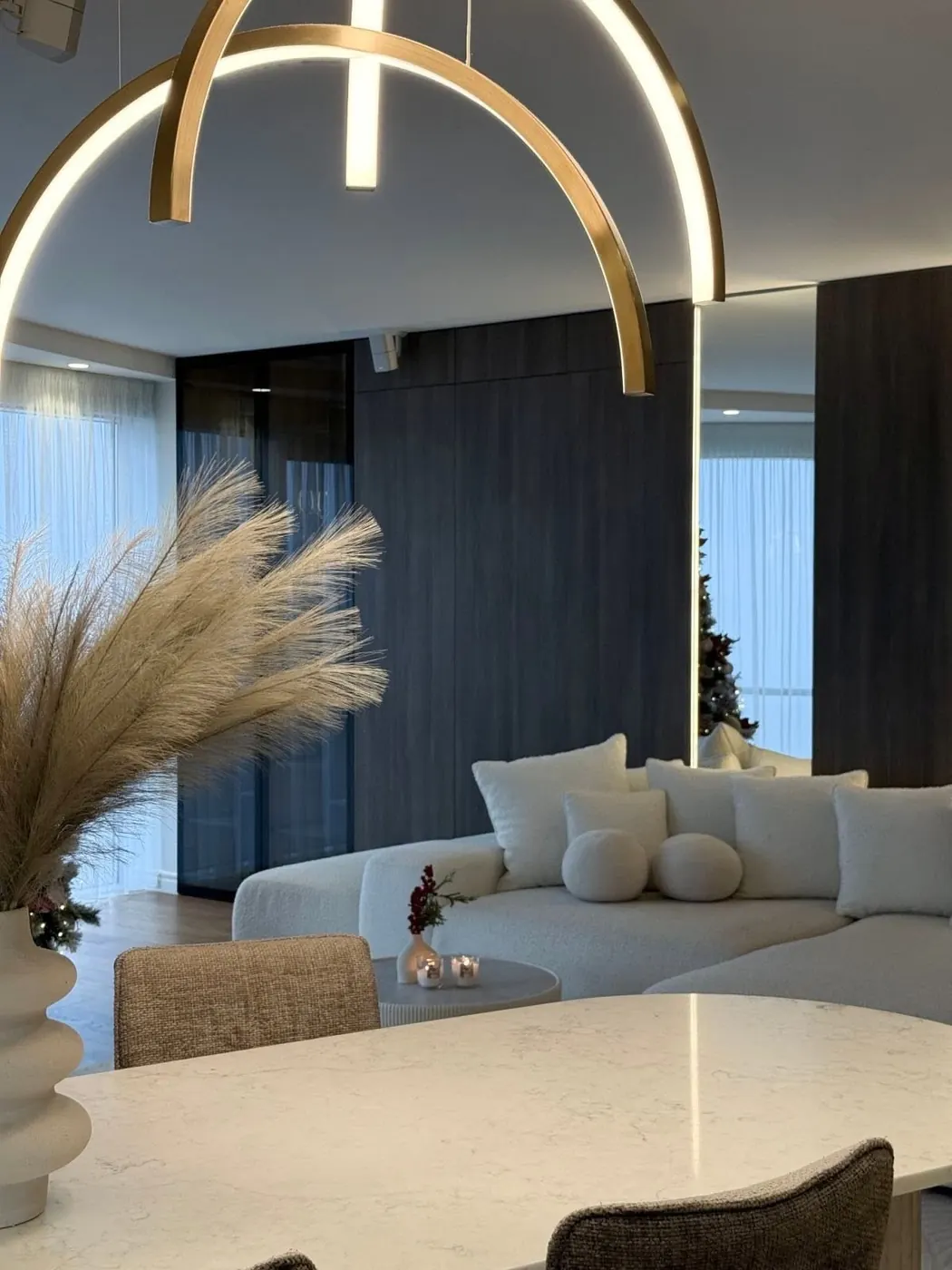 Svetainė su balta lenkta sofa ir apvaliu šviestuvu