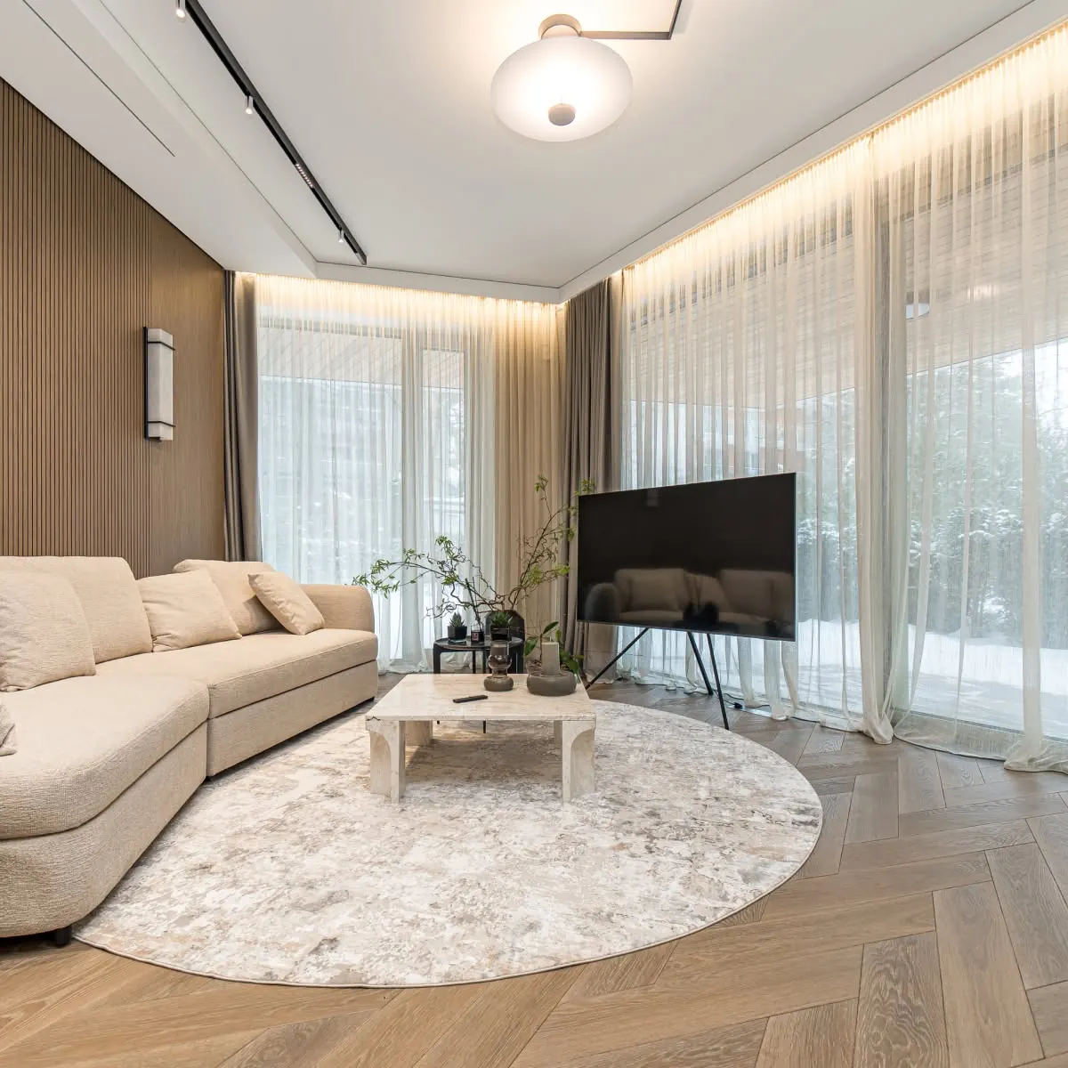 Svetainė su smėlio spalvos sofa ir apvaliu kilimu