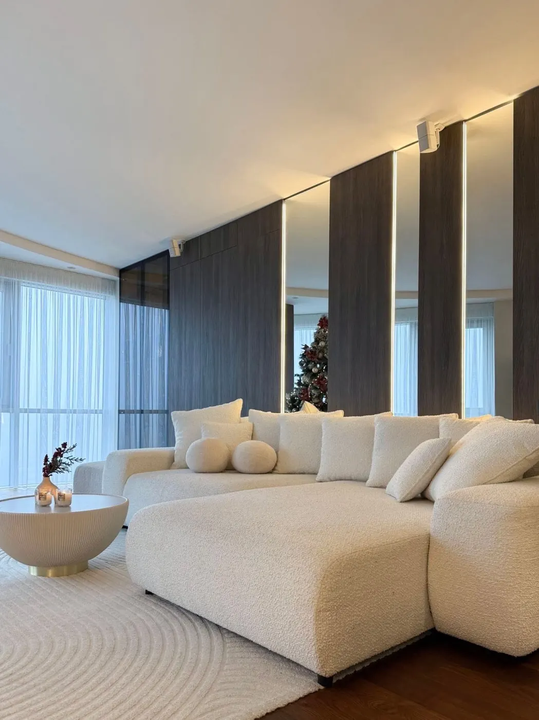 Svetainė su balta sofa ir tamsaus medžio panelėmis